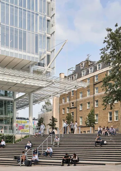 People relax on wide outdoor steps between a modern glass high-rise and a traditional brick building.