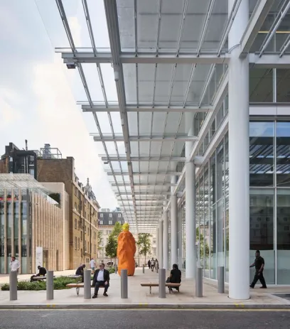 Modern glass skyscraper overlooking a busy public square with people walking and sitting on broad steps.
