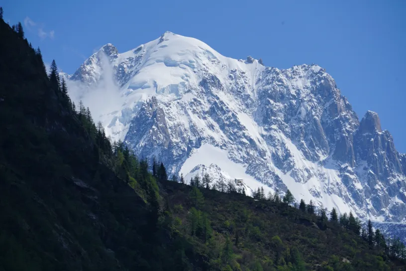 a snowy mountain with trees on the side and a blue sky in the background .