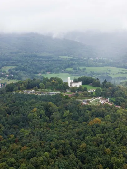 A white building sits on top of a hill surrounded by trees