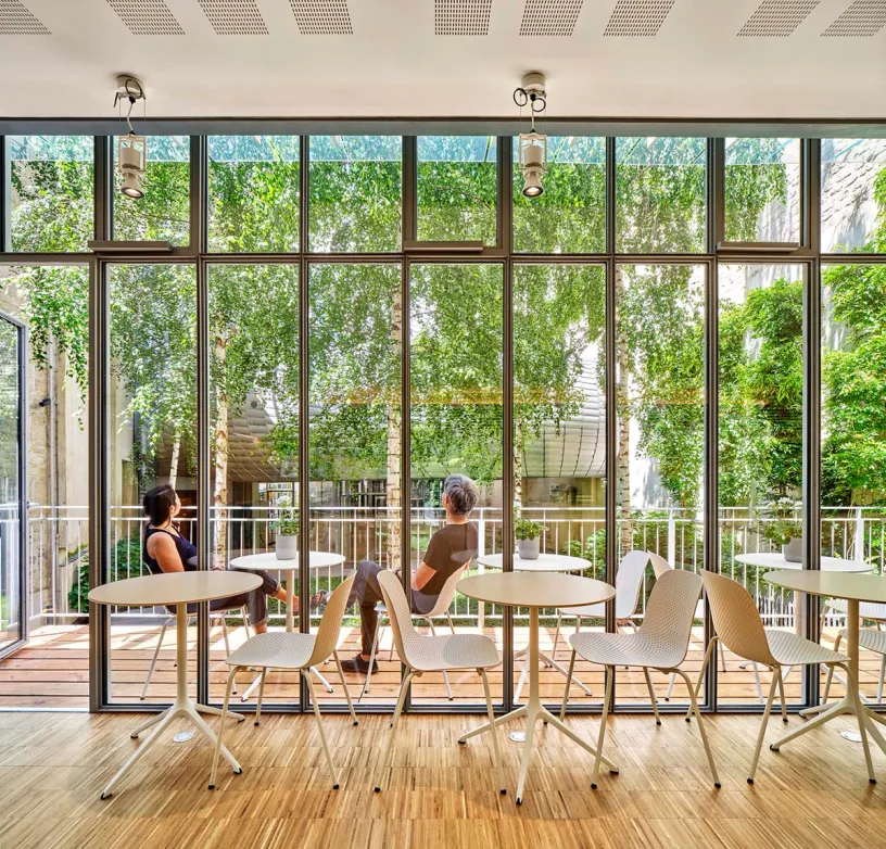 A couple of people are sitting at tables in front of a large window