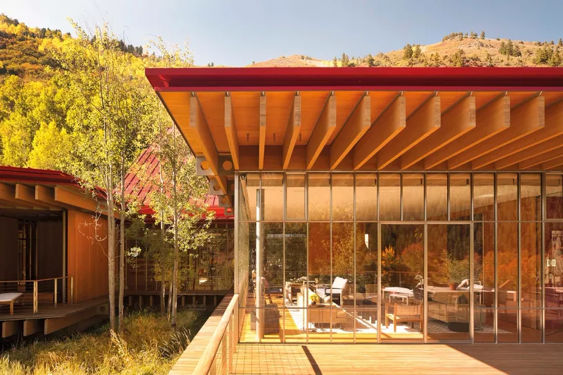 A modern wooden house with a red roof and lots of windows surrounded by trees