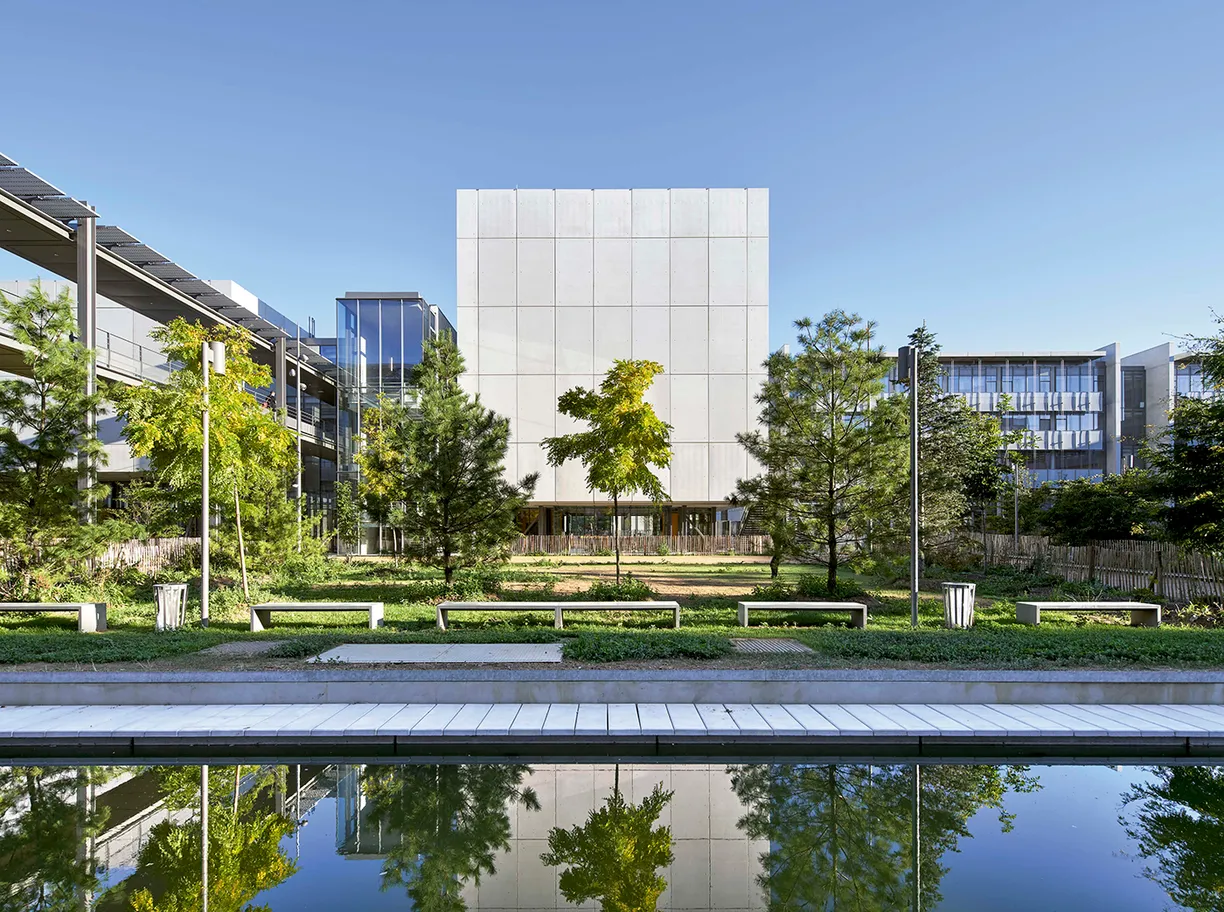 A large white building is surrounded by trees and a pond