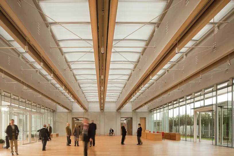A group of people are standing in a large room with a lot of windows