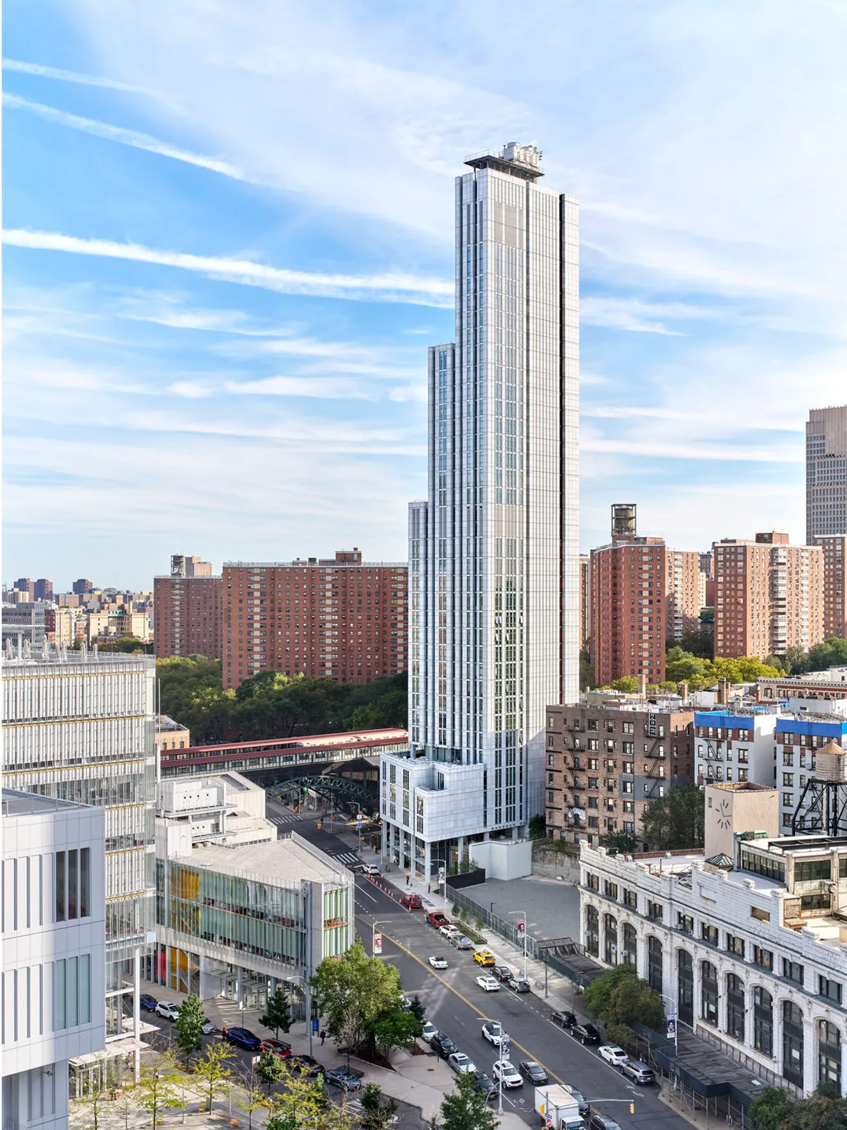 A towering modern white skyscraper dominates a cityscape with streets and various buildings under a blue sky.