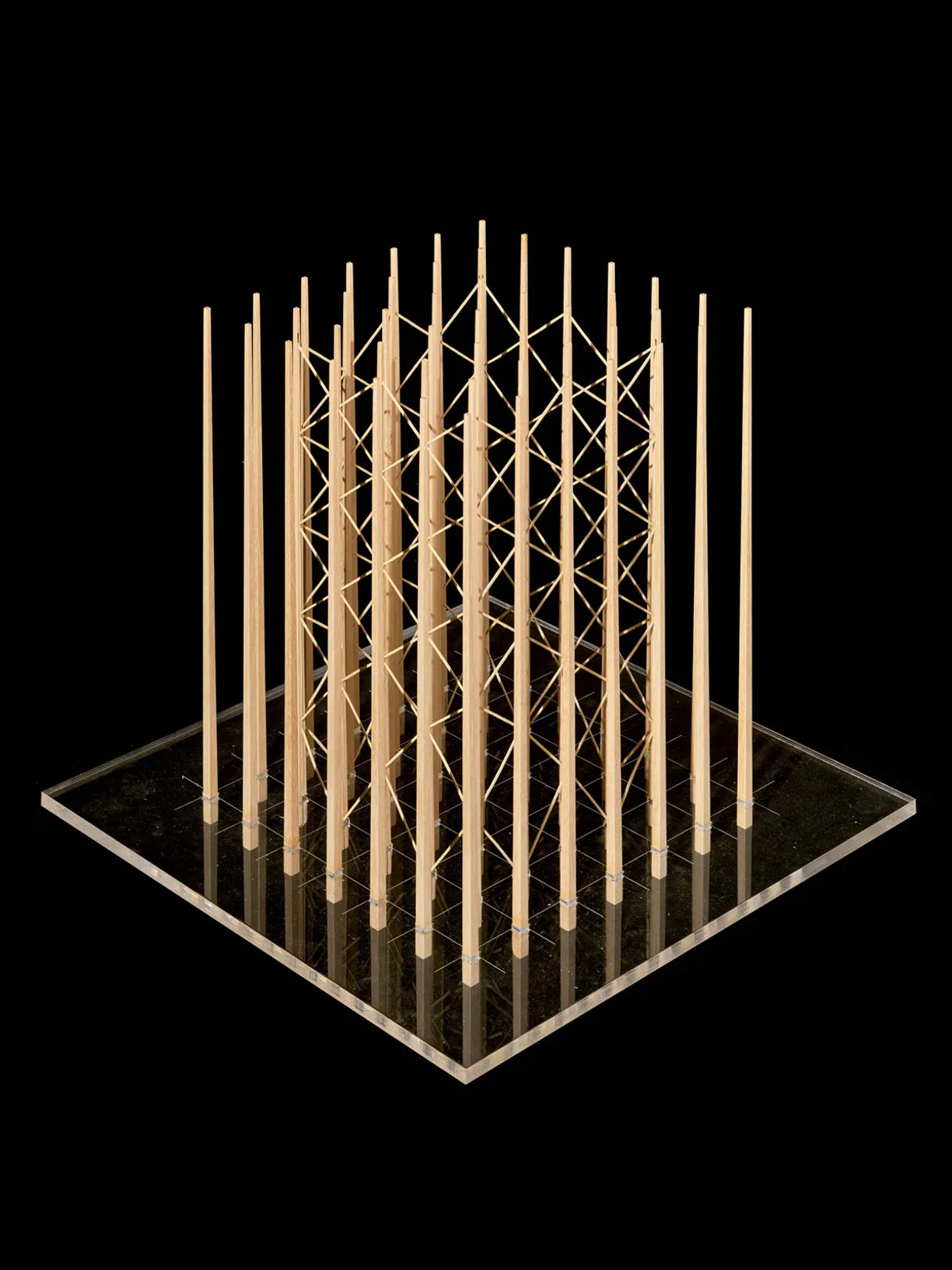 Architectural model with vertical wooden posts arranged in a grid on a clear base, braced by diagonal strings in the center.