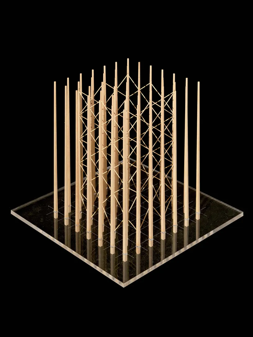 Architectural model with vertical wooden posts arranged in a grid on a clear base, braced by diagonal strings in the center.