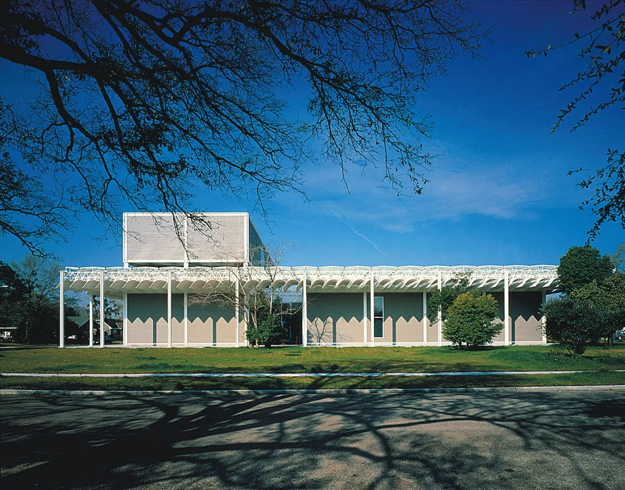 A large white building with a blue sky in the background is surrounded by trees