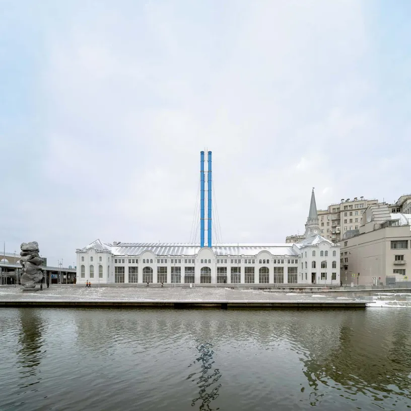 A large white building with two blue chimneys is next to a body of water