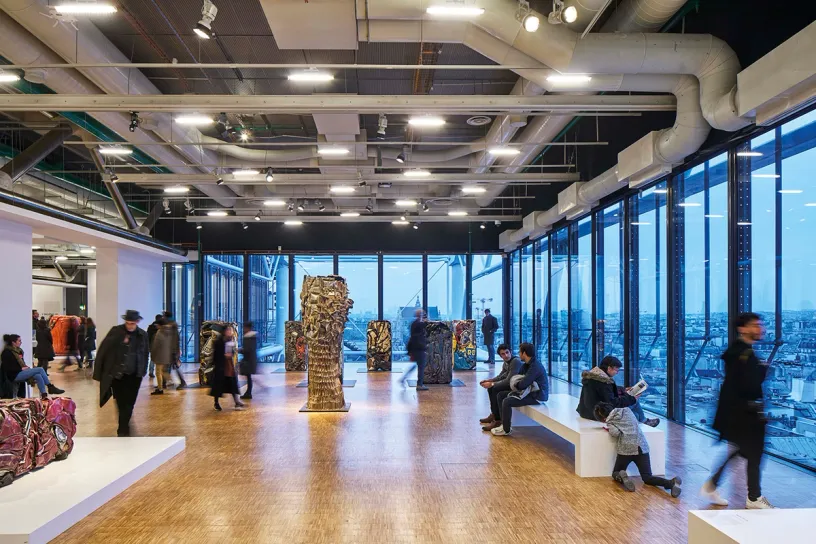 A large room with a lot of windows and people sitting on benches in it