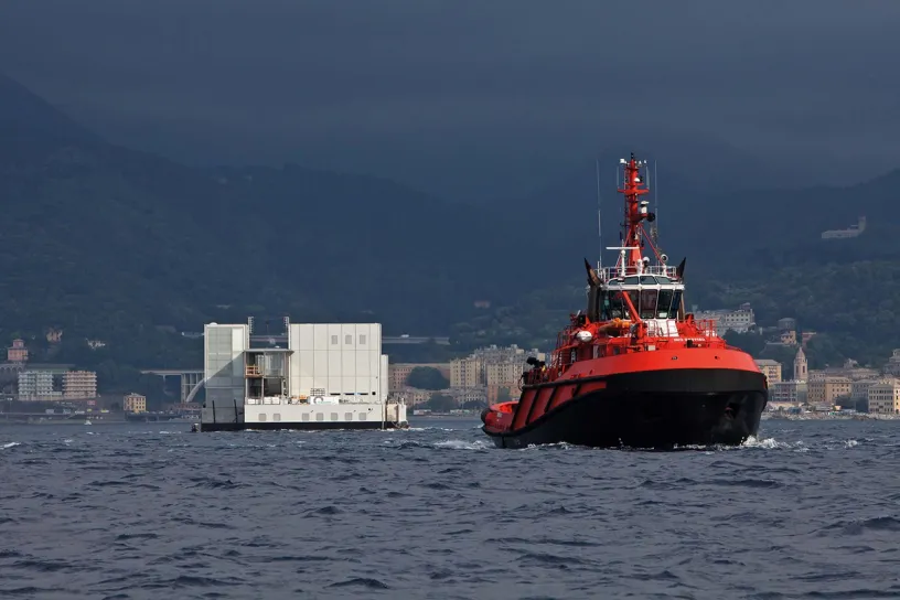 A tug boat is pulling a large floating object in the ocean