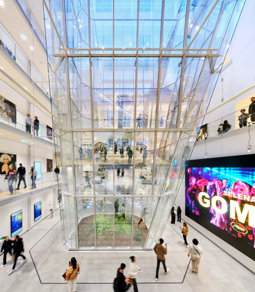 people are walking in a building with a screen that says selena gomez