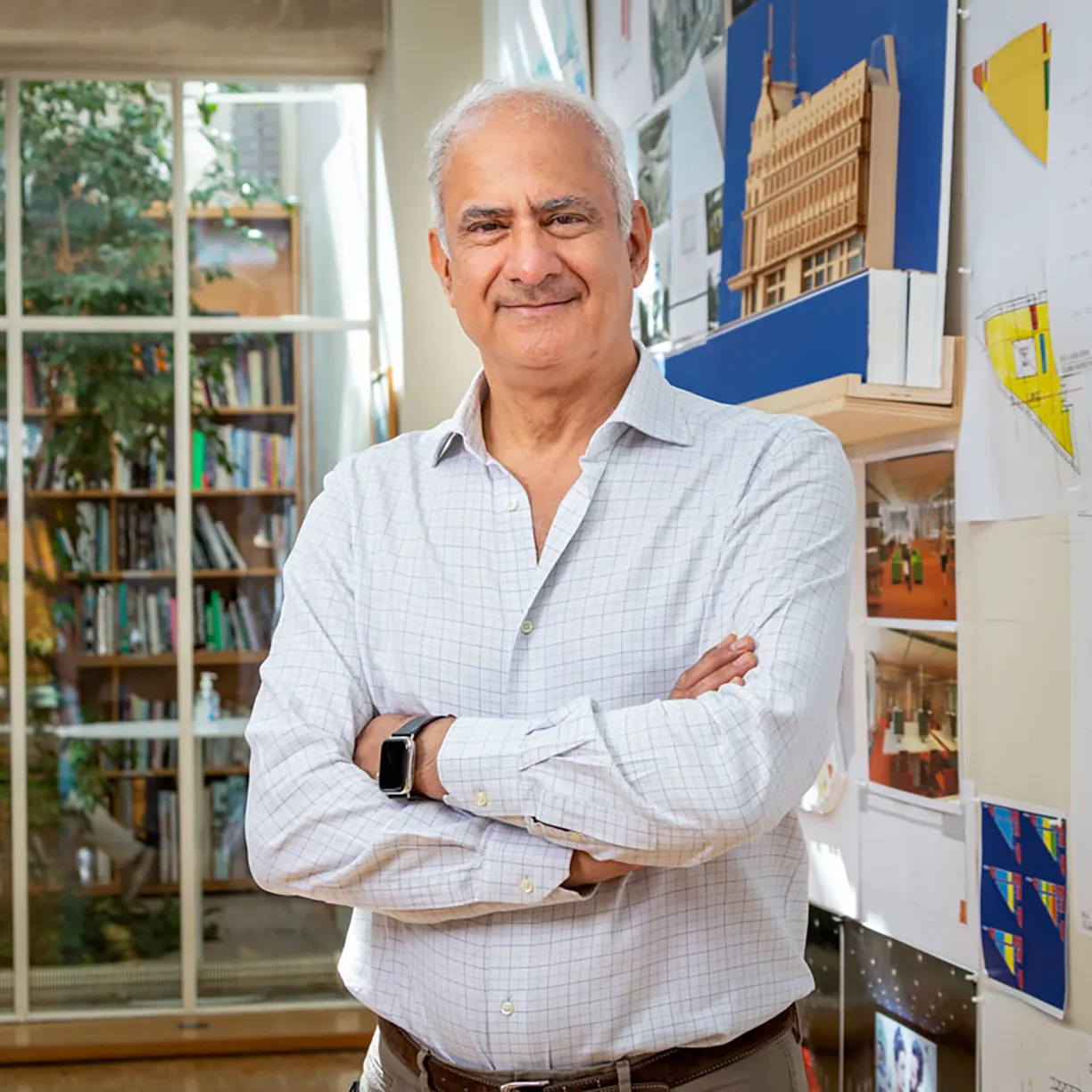 A man stands with his arms crossed in front of a wall with drawings on it