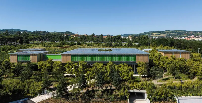 An aerial view of a large building with a green roof surrounded by trees