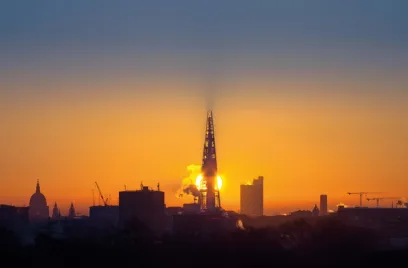 The sun is setting over a city skyline with a very tall building in the foreground