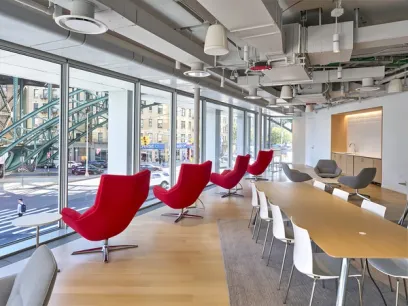 A modern conference room with two long white tables, red chairs, and tall windows on either side.