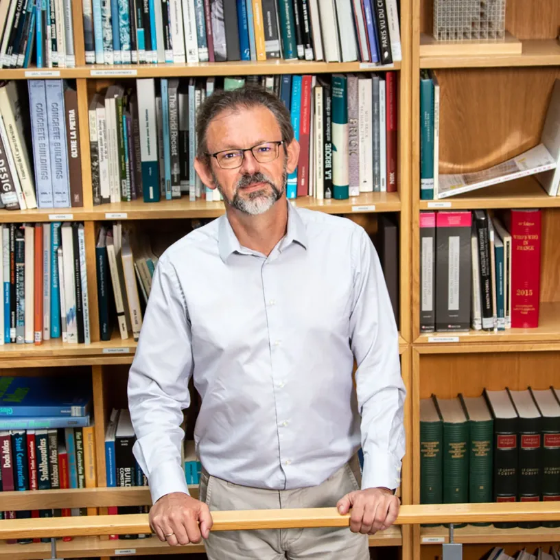 A man stands in front of a bookshelf holding onto a banister
