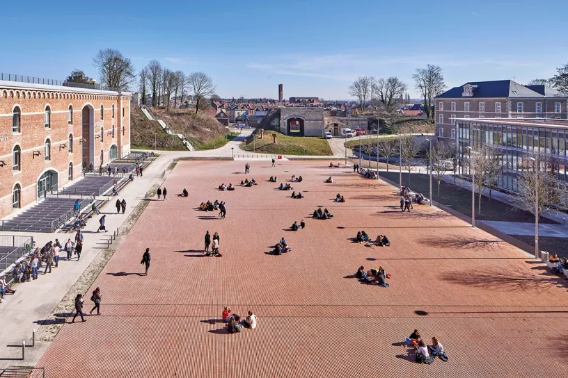 A group of people are sitting on the ground in a large square in front of a building