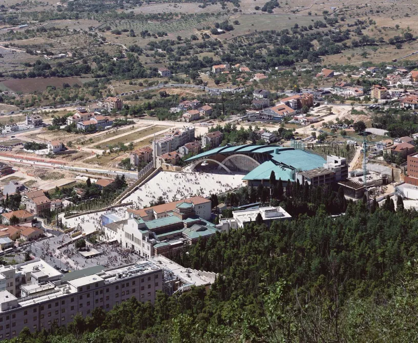 An aerial view of a large building in the middle of a city surrounded by trees