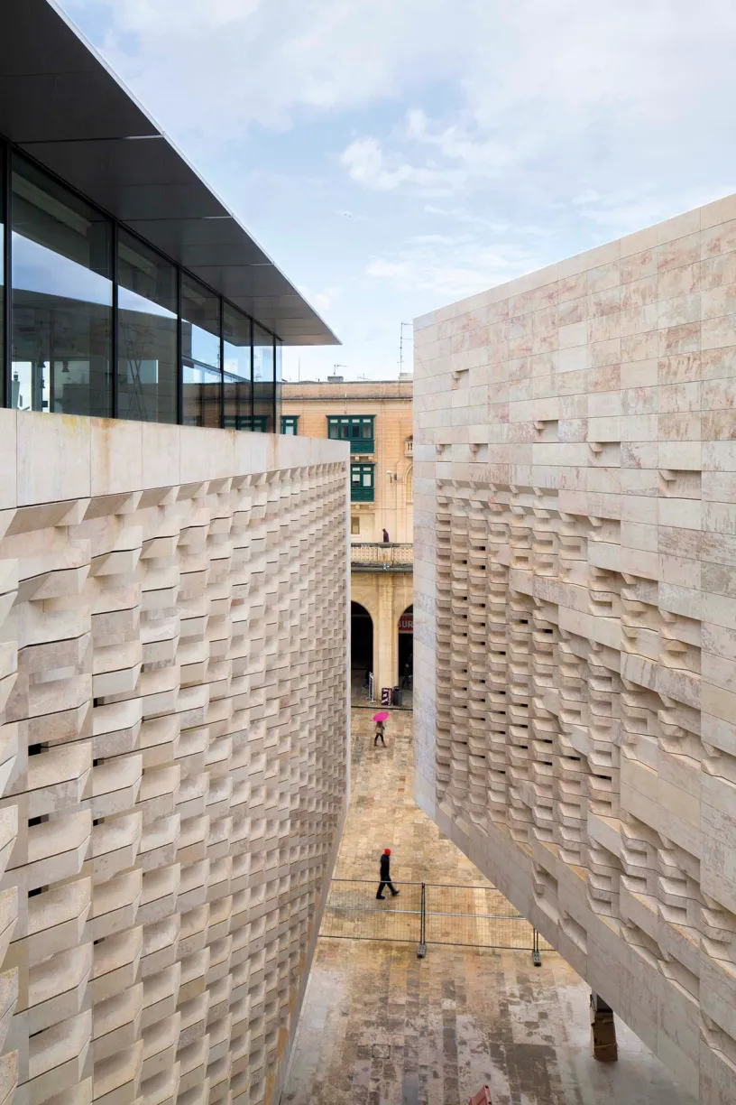 A man in a pink shirt walks between two buildings