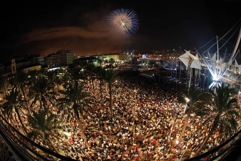 A large crowd of people are watching fireworks in a park at night