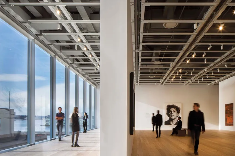 A group of people are standing in a large room with a lot of windows