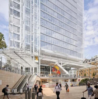 A modern glass skyscraper looms over a public plaza with escalators and a transparent canopy, where people walk past a colorful indoor sculpture.