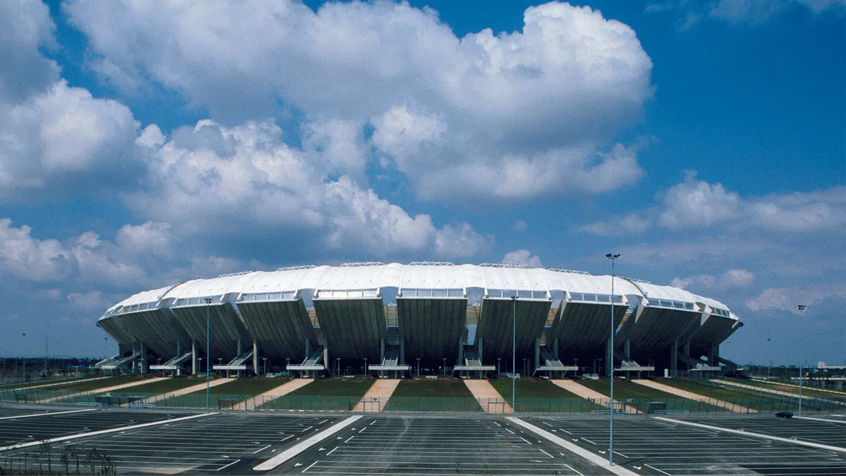 a large stadium with a parking lot in front of it on a cloudy day .