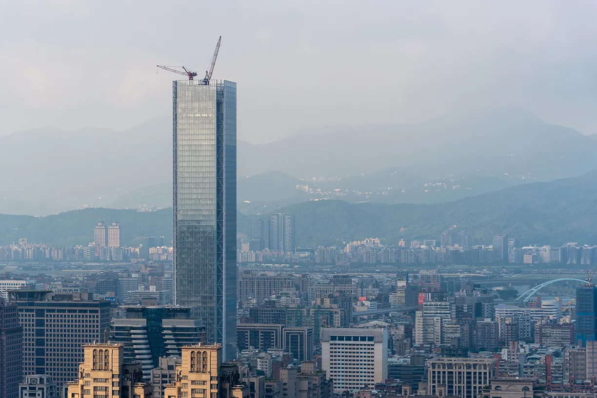 An aerial view of a city with a tall building under construction and mountains in the background