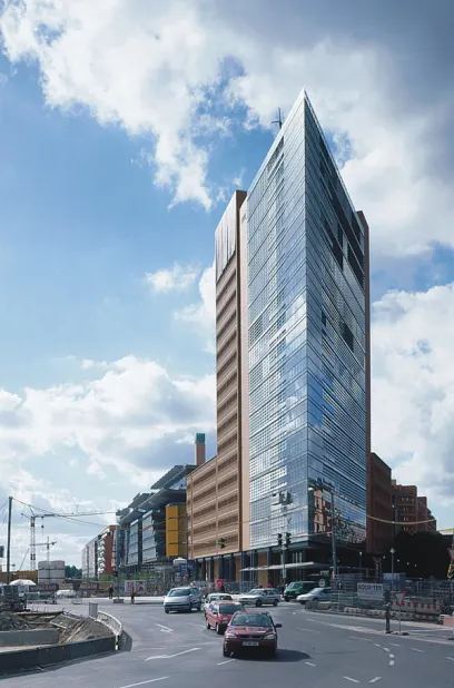 A red car is driving down a street in front of a tall building