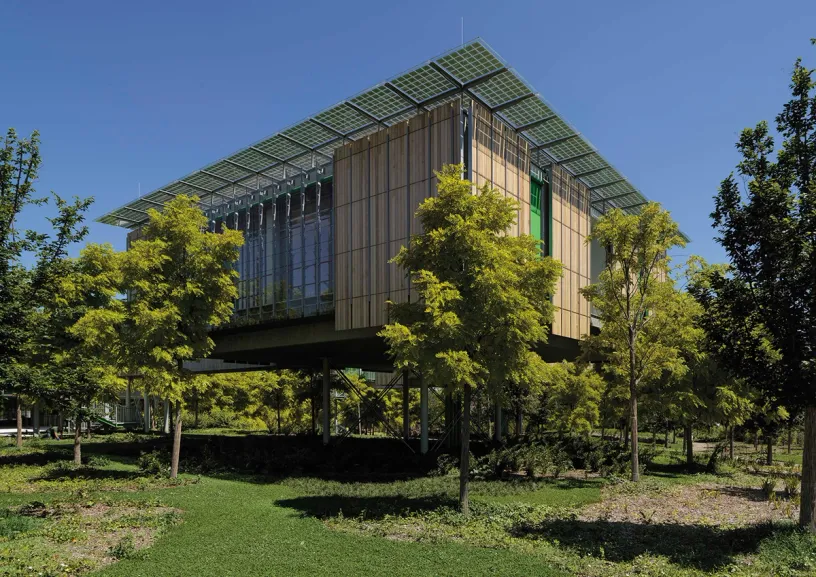 A large building with solar panels on the roof is surrounded by trees