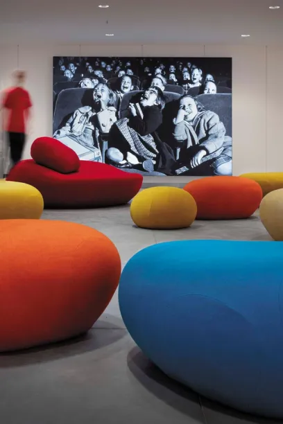 A group of colorful ottomans in front of a painting of people watching a movie