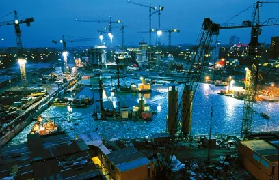A large construction site with cranes and boats in the water at night