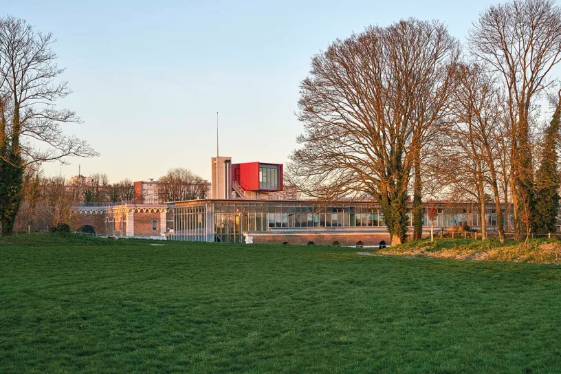 A large building is sitting in the middle of a grassy field surrounded by trees