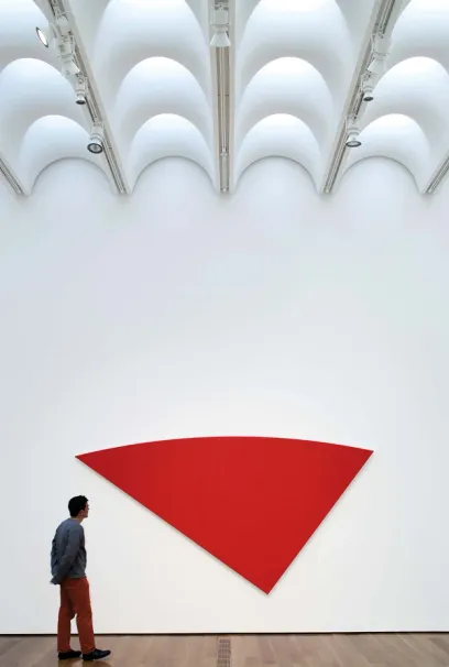 A man looks at a large red triangle on a white wall