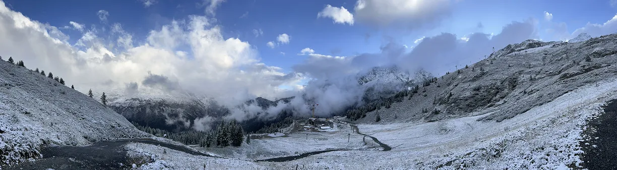 a panoramic view of a snowy mountain valley with a blue sky and clouds .