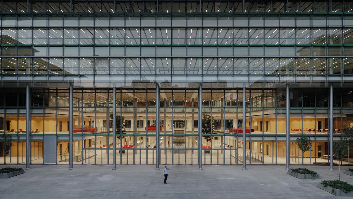 A man is standing in front of a large building with a lot of windows