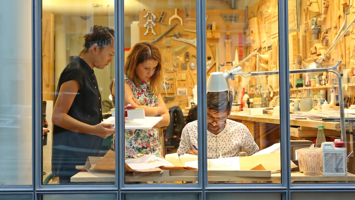 a group of people are working in a workshop behind a glass wall .