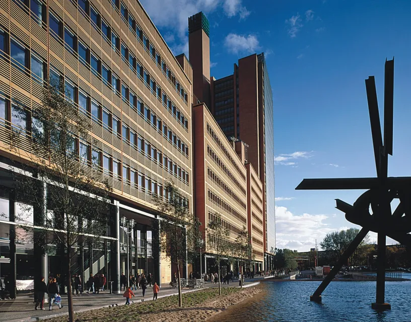 A group of people are walking in front of a large building next to a body of water