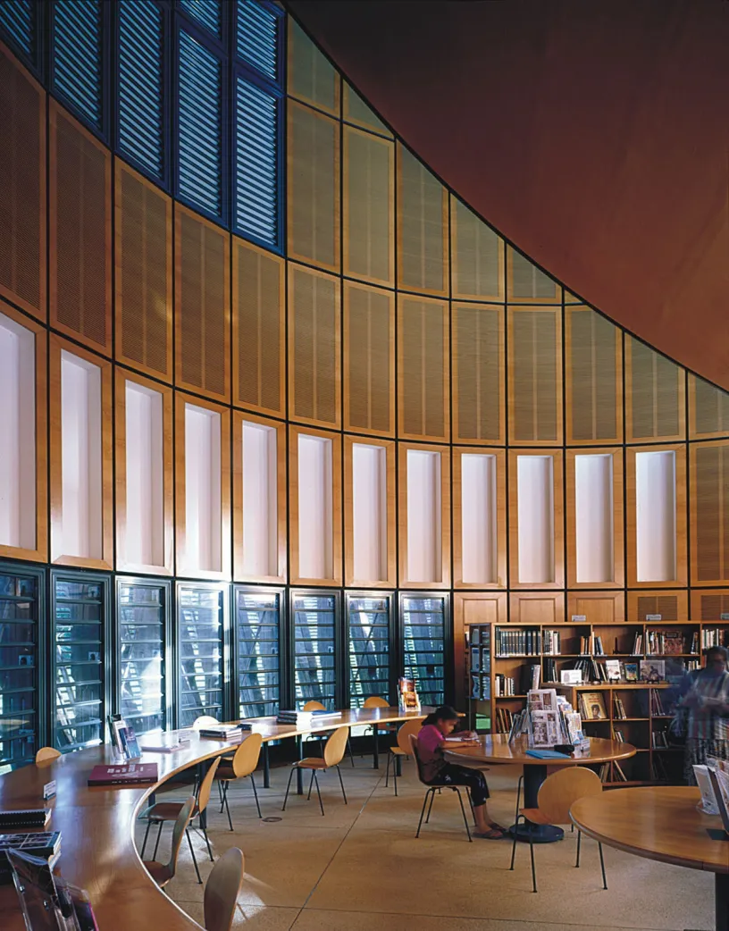 A woman sits at a table in a library reading a book