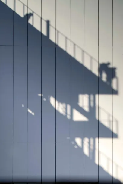 A shadow of a person standing on top of a building is cast on a wall