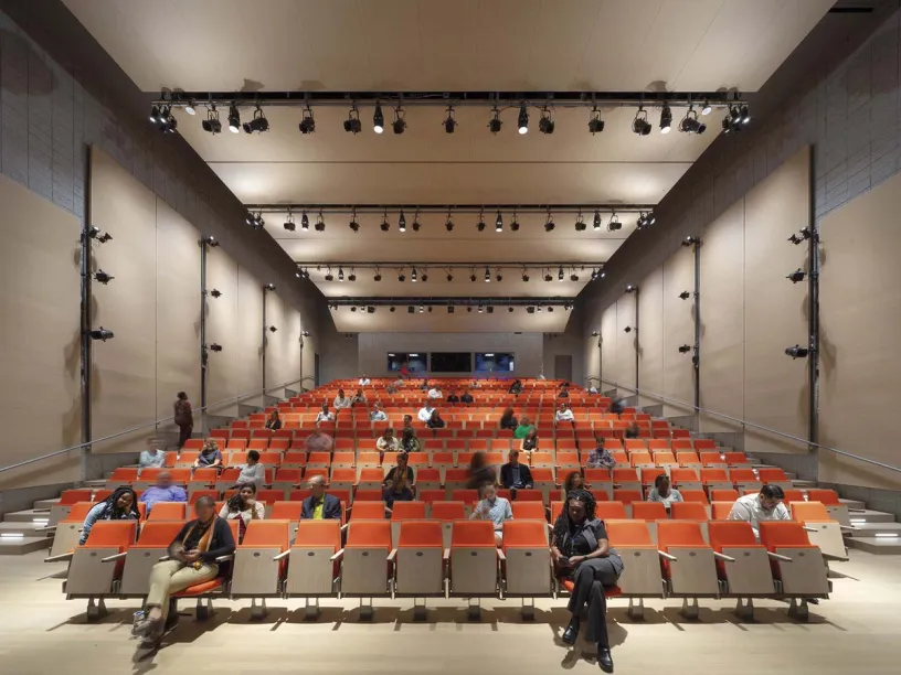 a large auditorium filled with people sitting in orange chairs .