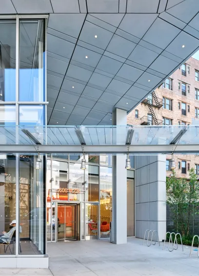 Aerial view of a modern high-rise building with a rooftop terrace, green space, and elevated train tracks in the background.