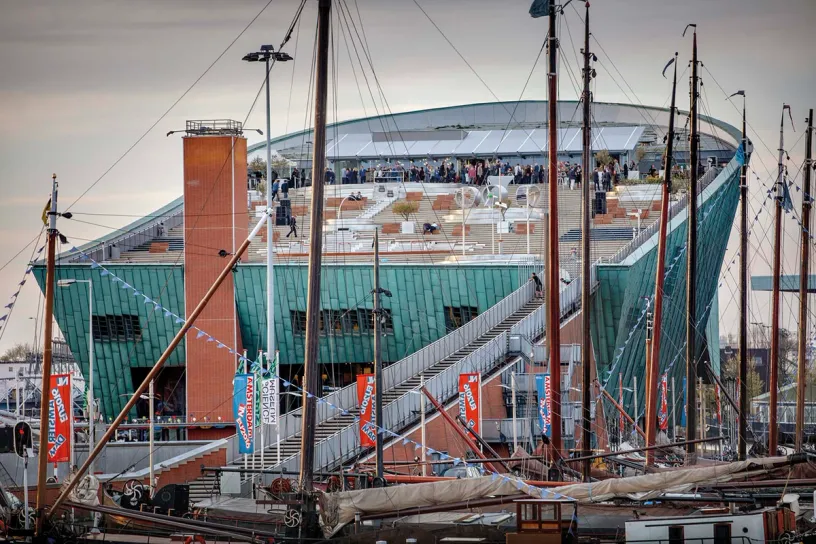 A group of sailboats are docked in front of a large building