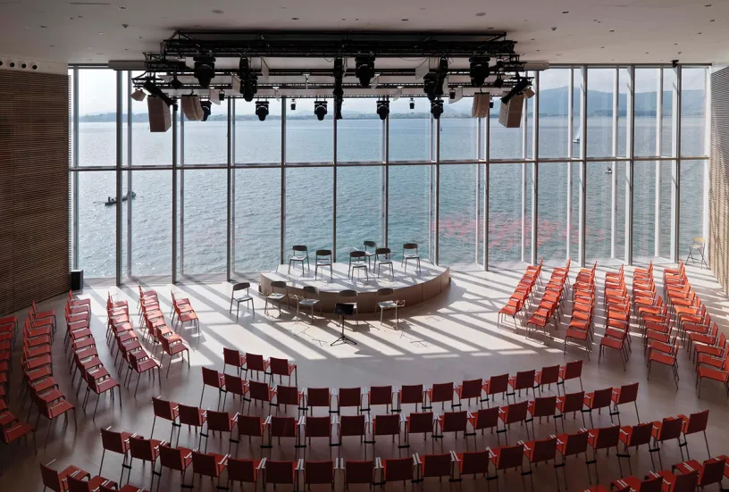 A large auditorium filled with red chairs and a stage with a view of the ocean