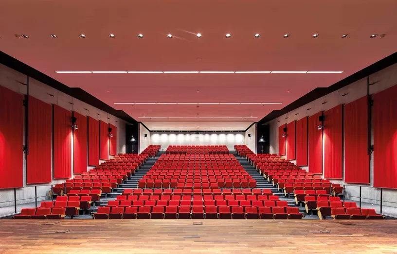 A large auditorium filled with red seats and a wooden stage