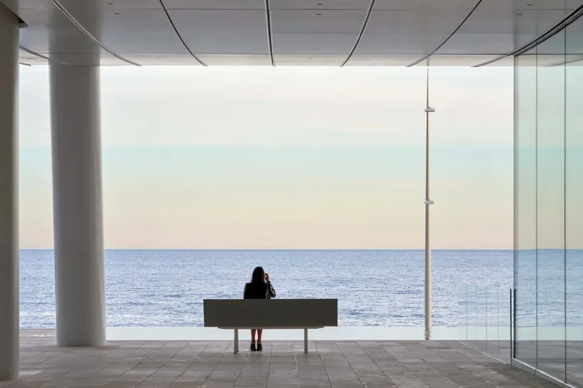A woman is sitting on a bench looking out over the ocean