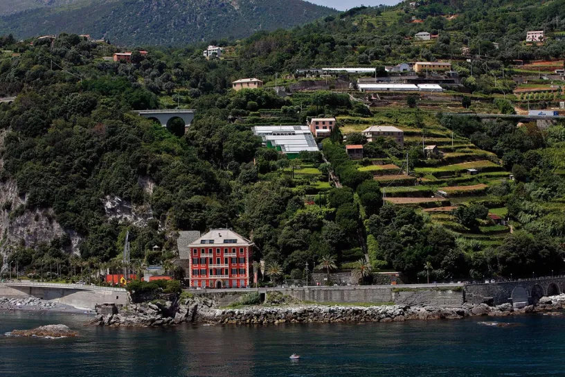 A large red building is sitting on top of a hill next to a body of water