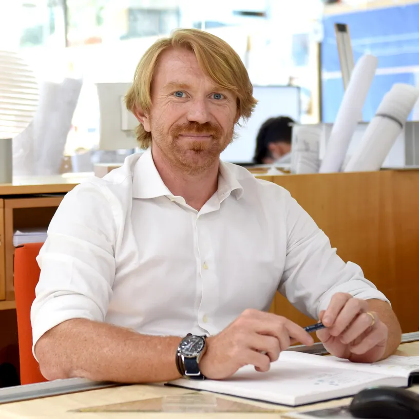 A man wearing a watch sits at a desk