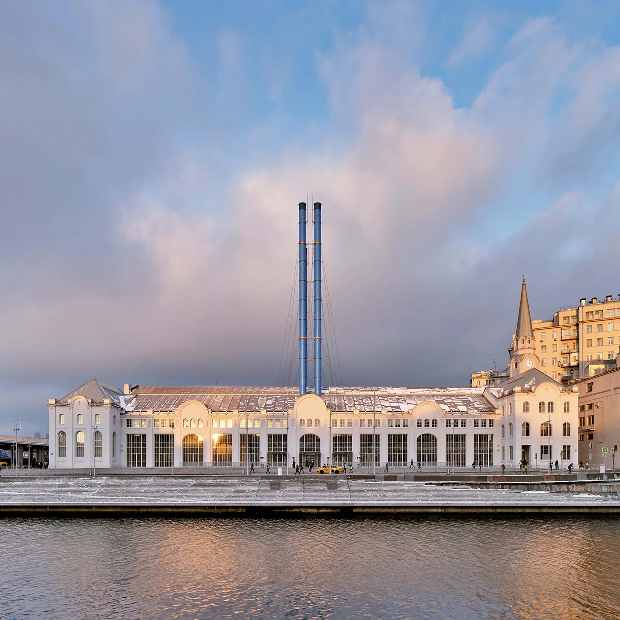 A large white building with two chimneys on the side of it is next to a river